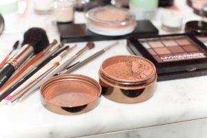 open bronzer powder on a marble counter with makeup brushes in the background